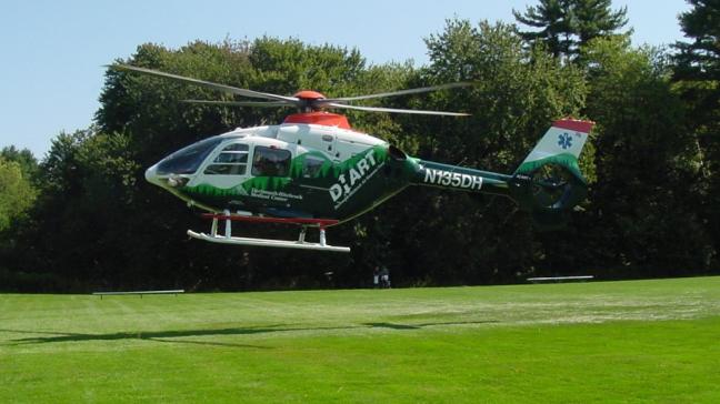 A DHART helicopter lands on a field.