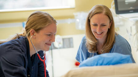 Two nurses looking at and listening to their patient in a hospital bed